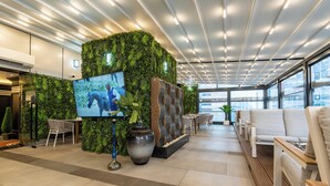 A modern lobby with a green wall, a large TV, and a seating area with white sofas and wooden tables. - Samaya Hotel Deira (Dubai)