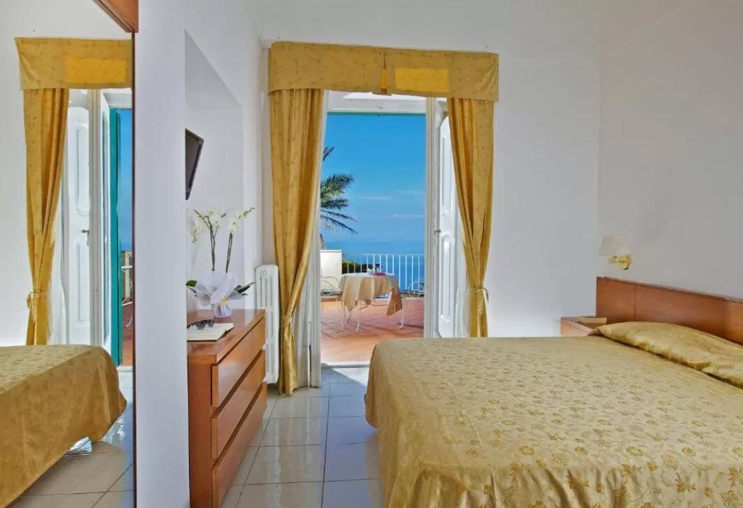 Een hotelkamer met twee bedden, een houten dressoir en uitzicht op zee.
