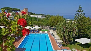 A swimming pool with lounge chairs and umbrellas, surrounded by greenery and buildings. - Hotel San Michele (Anacapri)