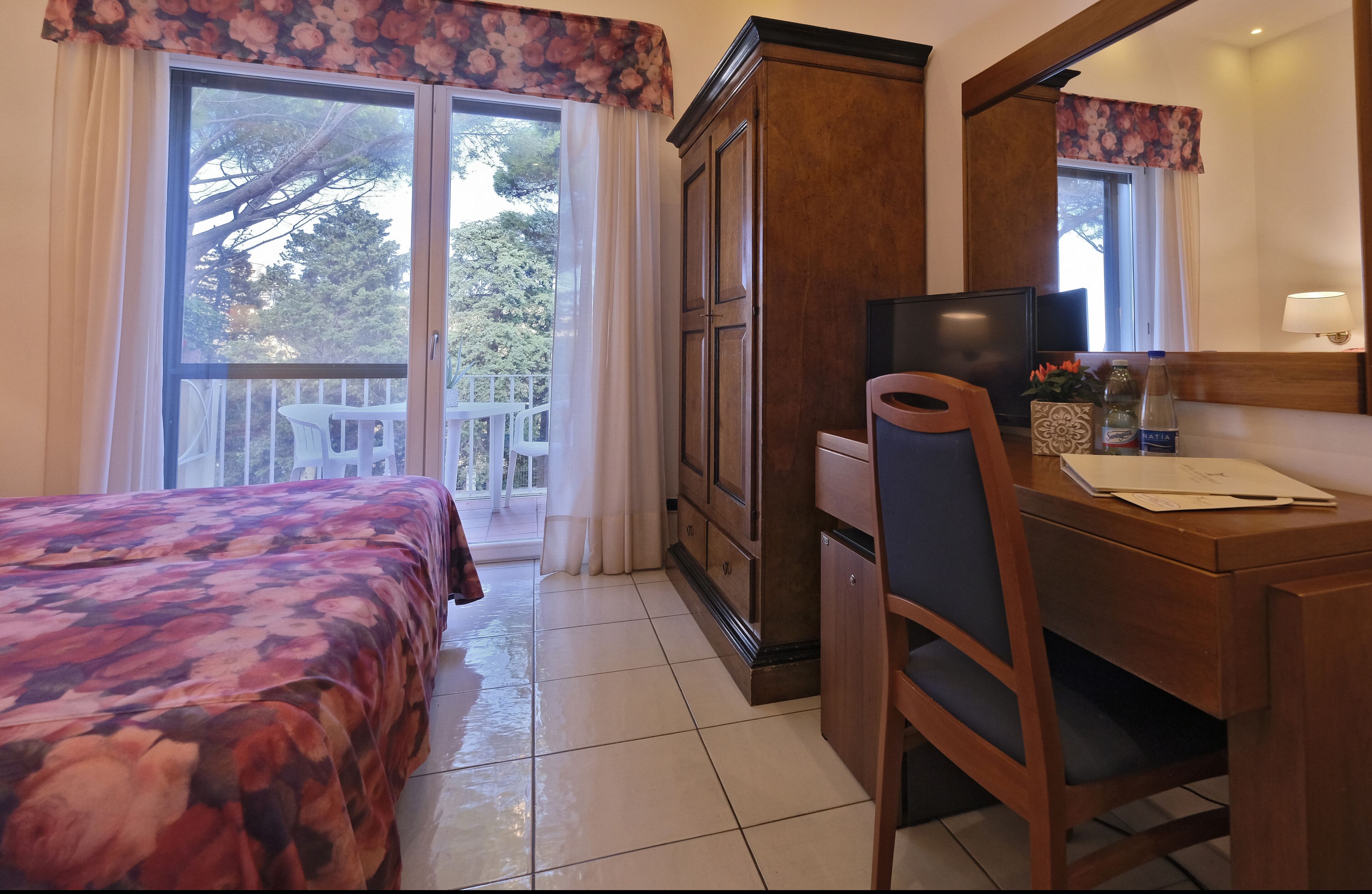 A hotel room with a bed, a desk, a chair, a television, and a window with curtains.