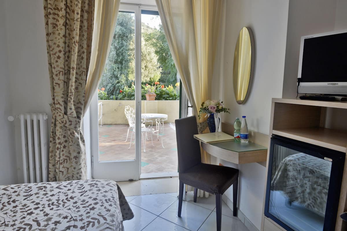 Ein Hotelzimmer mit Bett, Schreibtisch mit Stuhl, Fernseher und Blick auf die Terrasse.