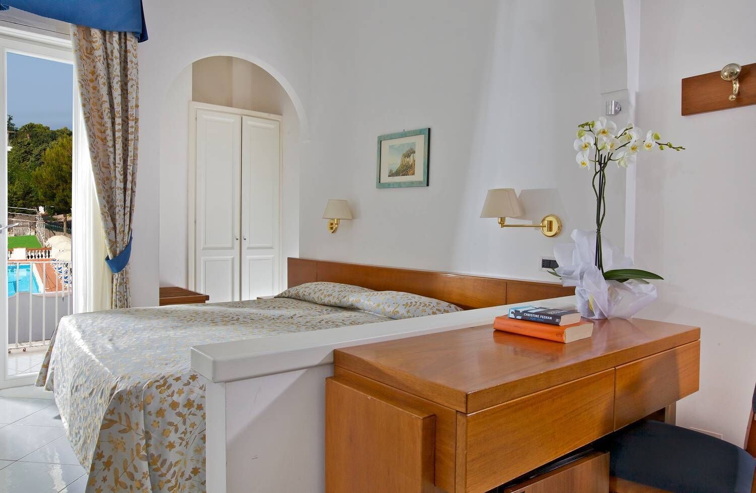 Habitación de hotel con cama, mesita de noche, lámpara y vista al exterior.
