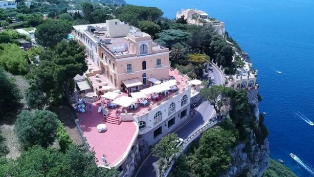 An aerial view of a coastal hotel with a red-roofed terrace, a stone facade, and a view of the sea. - Hotel San Michele (Anacapri)