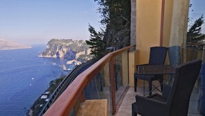 A balcony with a view of the sea and cliffs, furnished with wicker chairs and a table. - Hotel San Michele (Anacapri)
