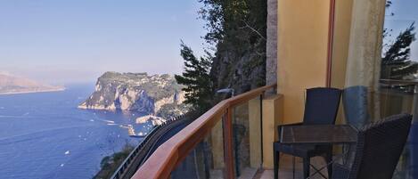 Un balcon offrant une vue sur la mer et les falaises, aménagé avec des fauteuils et une table en osier.