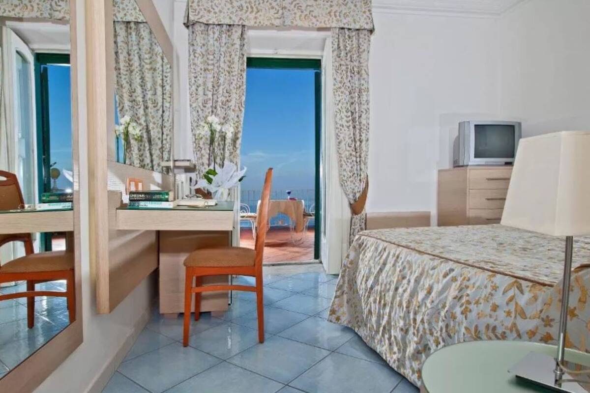 Ein Hotelzimmer mit Bett, Schreibtisch, Stuhl, Fernseher und Meerblick durch das Fenster.