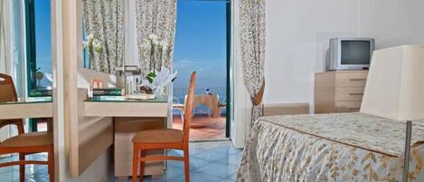 Une chambre d’hôtel équipée d’un lit, d’un bureau, d’une chaise, d’une télévision et offrant une vue sur la mer par la fenêtre.