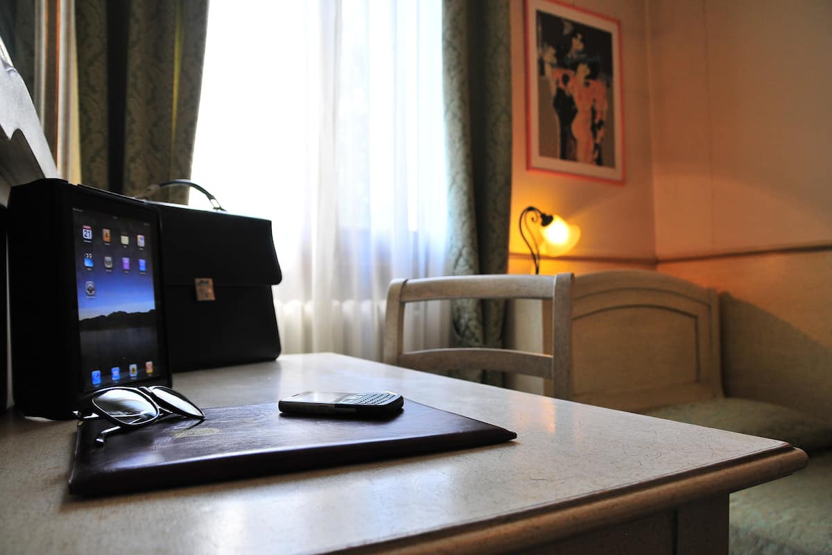 A hotel room with a wooden table, a laptop, a smartphone, and a pair of glasses.