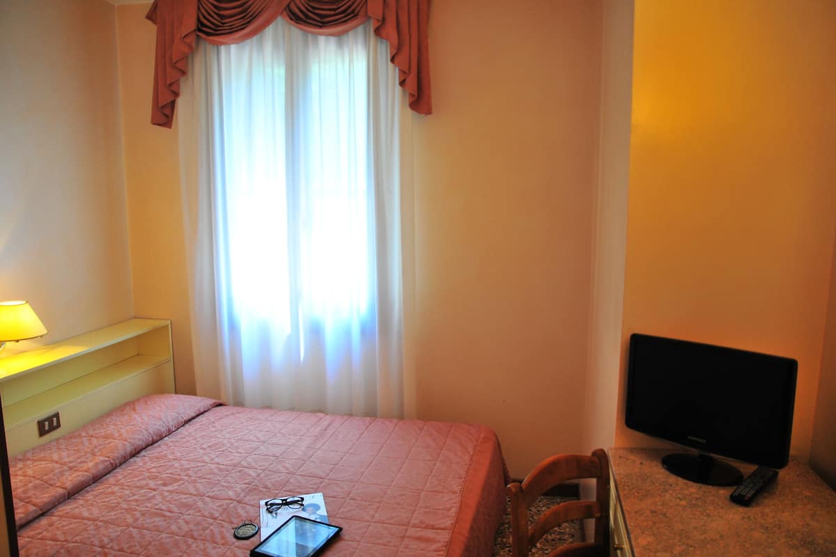 A hotel room with a bed, a television, a desk with a lamp, and a window with curtains.