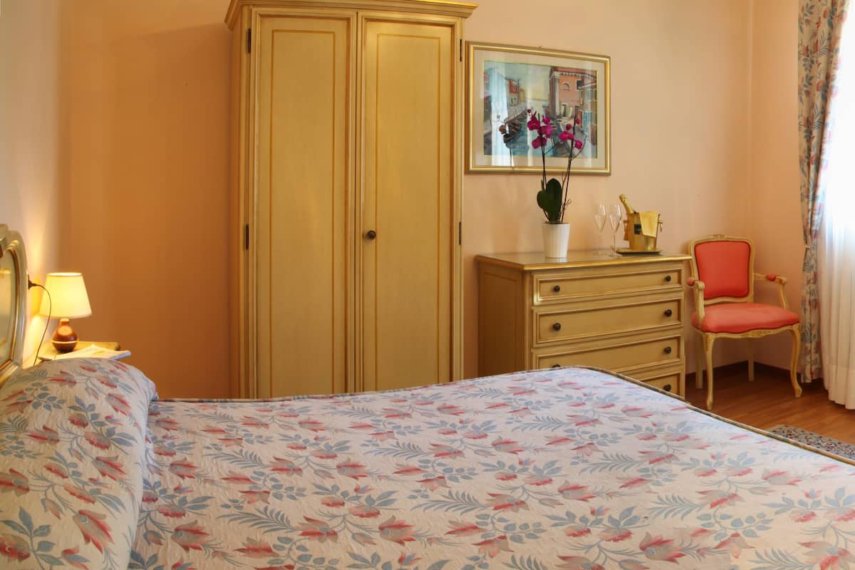 A hotel room with a bed, a desk, a chair, a television, and a wardrobe.