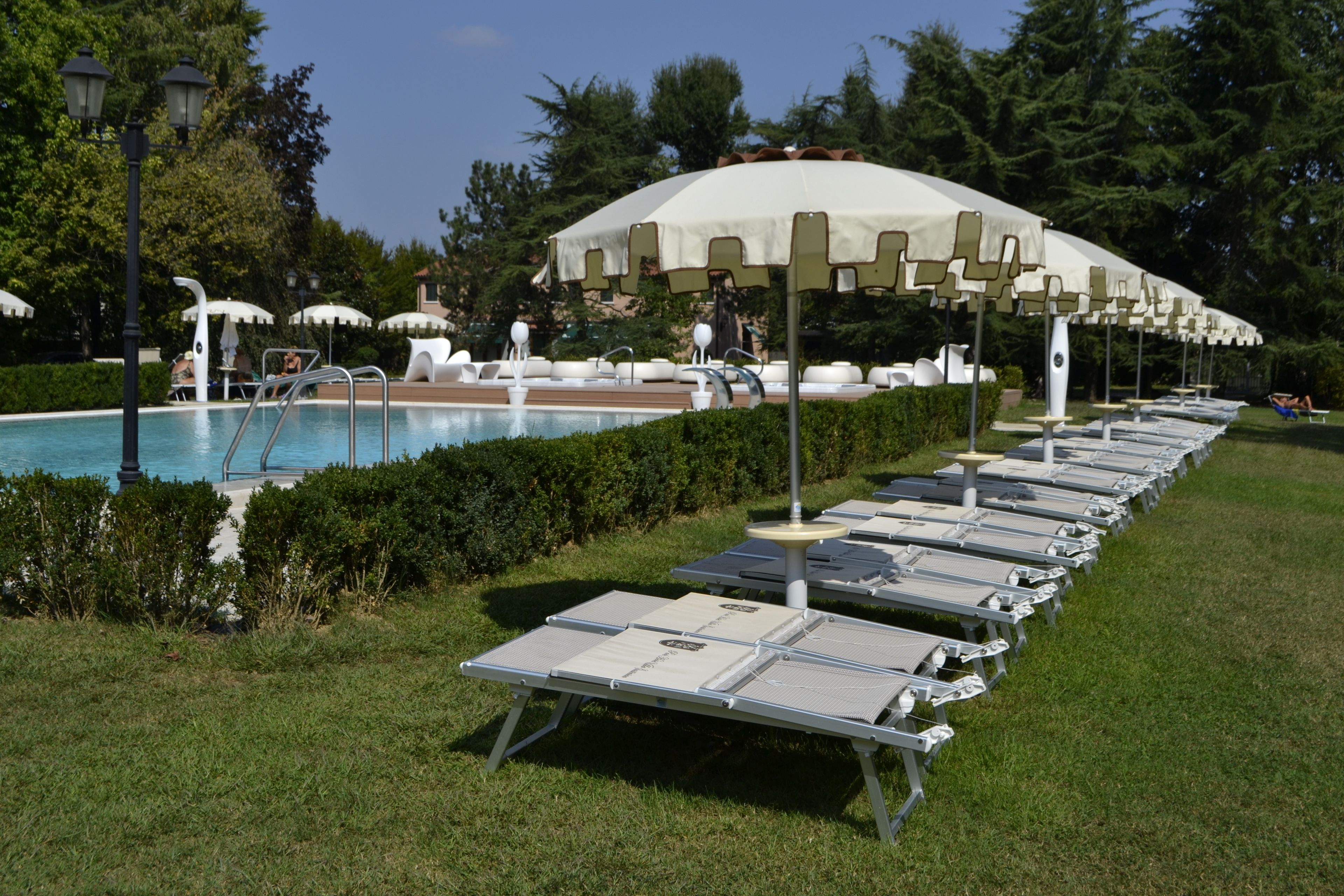 Zona junto a la piscina con sillones reclinables y sombrillas, rodeada de vegetación.