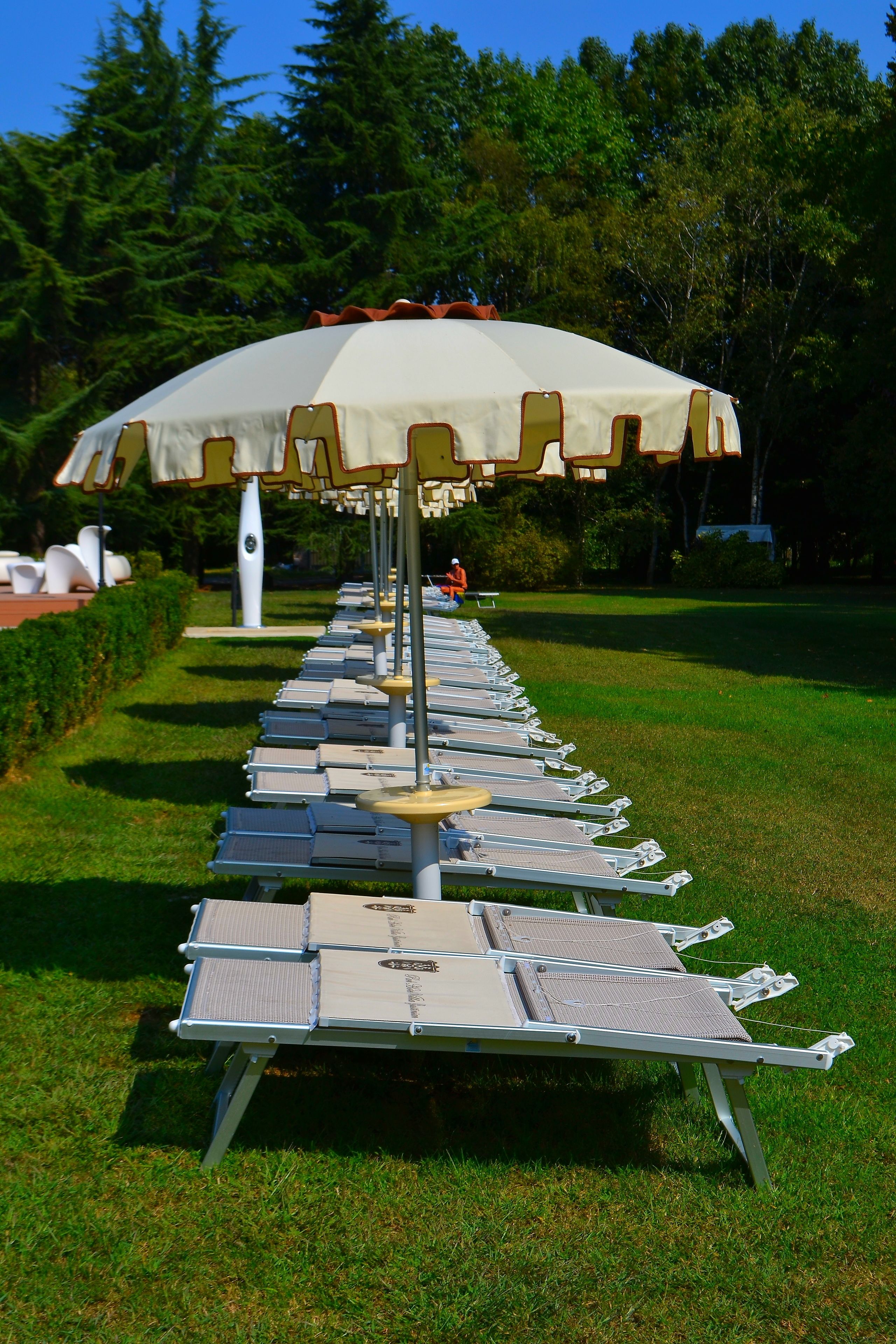 A row of sun loungers with umbrellas in a grassy outdoor area.