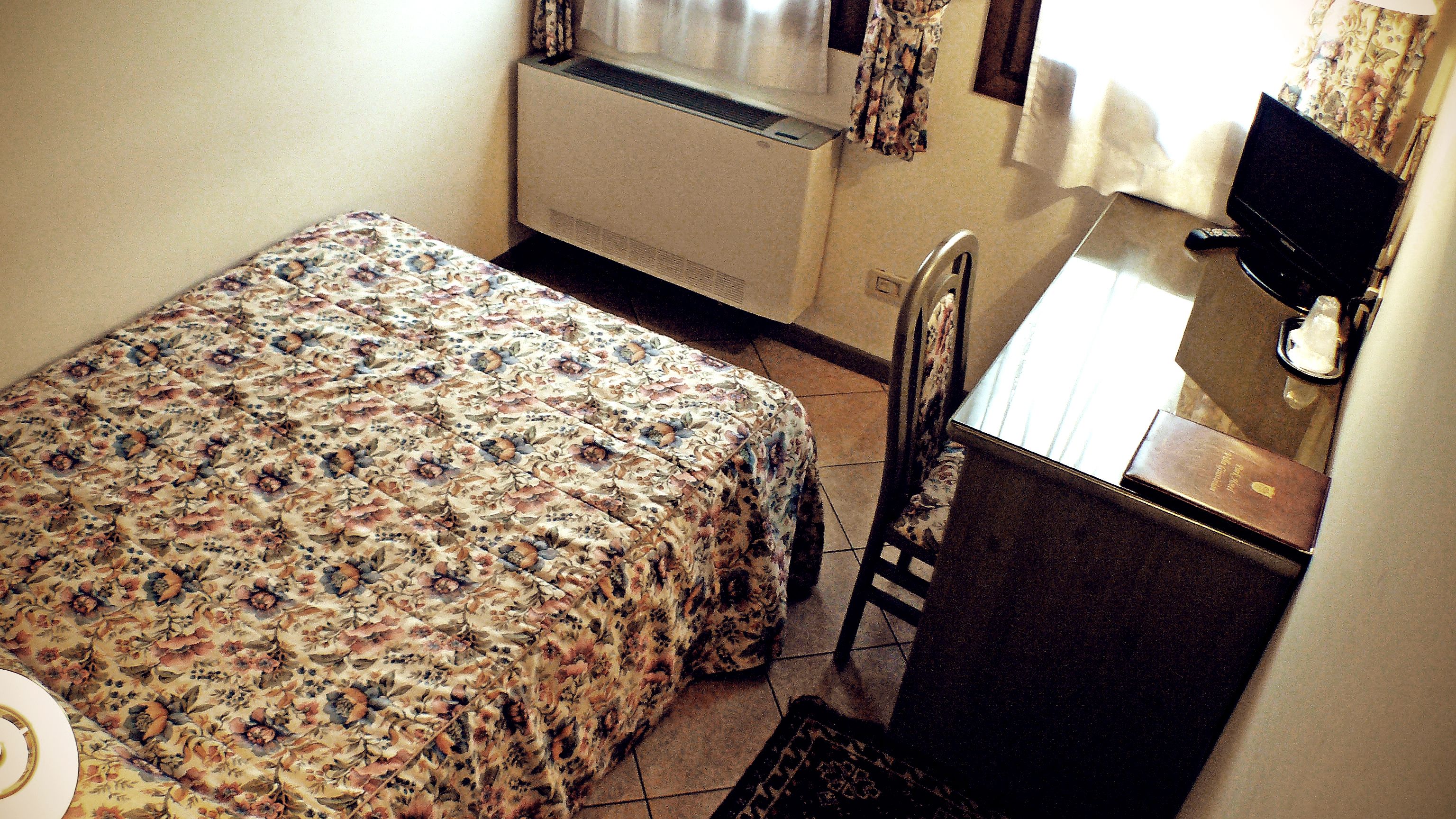 A small, neatly arranged room with a bed, a desk, and a chair.