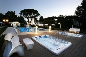 A pool area with hot tubs and lounge chairs, surrounded by trees and buildings. - Park Hotel Villa Giustinian (Mirano)