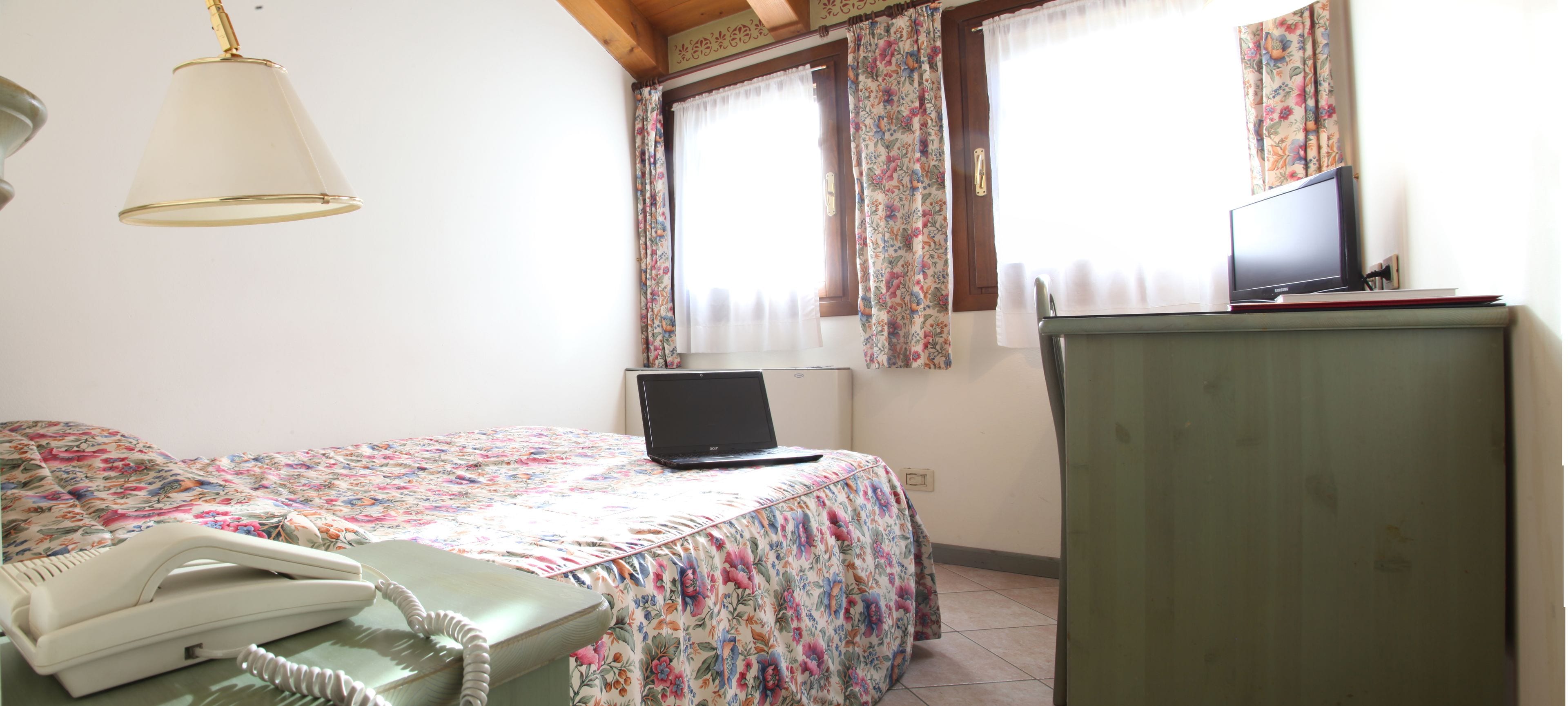 Ein Schlafzimmer mit einem Bett, einem Schreibtisch mit Laptop, einem Telefon und einem Fernseher auf einer Kommode.