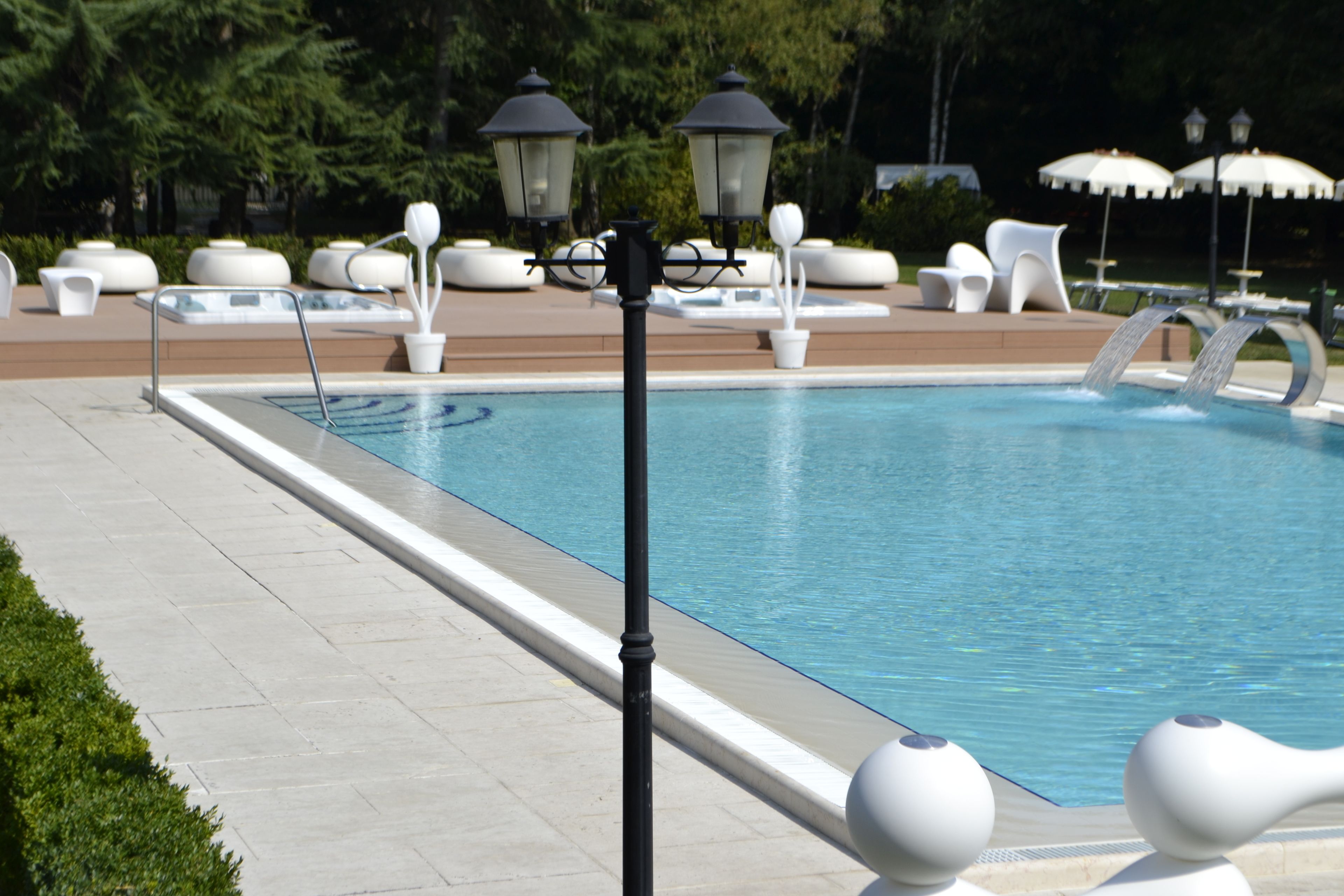 A swimming pool with a water feature, surrounded by lounge chairs and tables, and lamp posts.