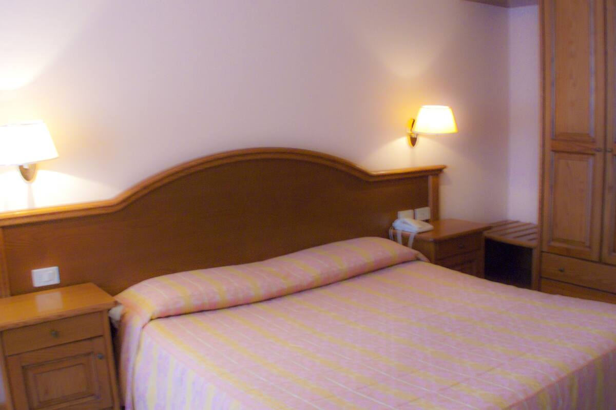 A hotel room with a single bed, bedside lamps, a nightstand, a telephone, and wooden wardrobe doors.