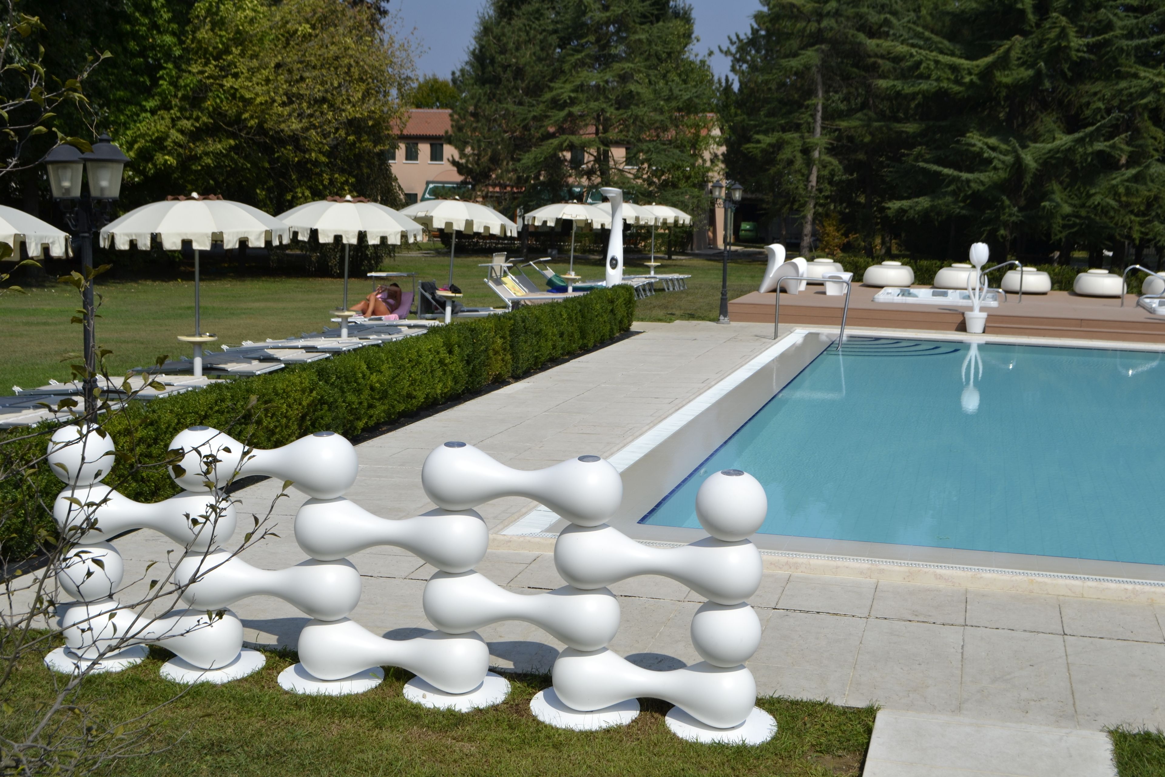 Une piscine entourée de verdure et agrémentée d’une sculpture originale, avec des chaises longues et des parasols à proximité.