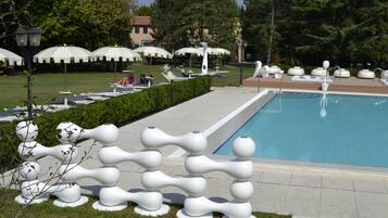Una piscina con lettini e ombrelloni, immersa nel verde e con una scultura originale.