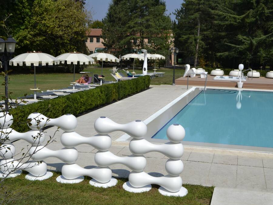 Una piscina con lettini e ombrelloni, immersa nel verde e con una scultura originale.