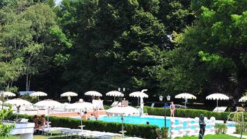 Area piscina con sedie a sdraio e ombrelloni, immersa nel verde.