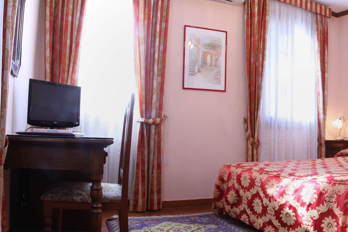 A hotel room with a bed, a desk with a television, a chair, and two framed pictures on the wall.