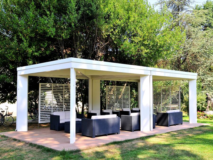 A covered outdoor seating area with sofas and a table, surrounded by trees.