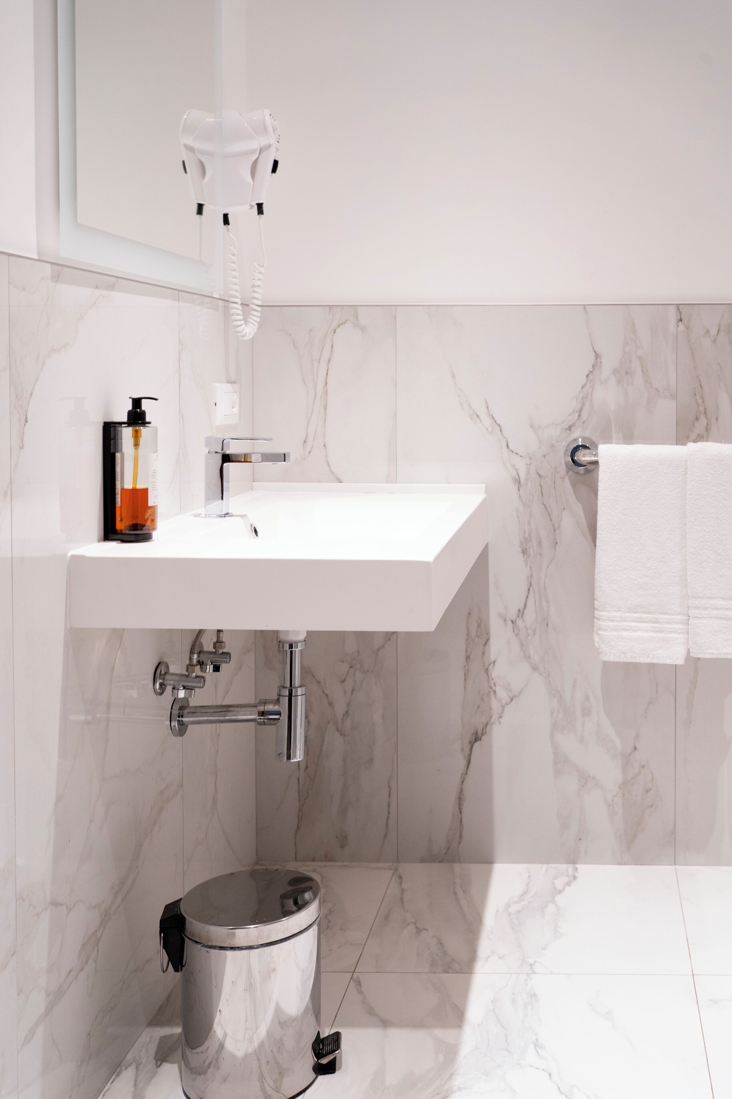 Ein Badezimmer mit einem weißen Waschbecken, einem an der Wand montierten Föhn, einer Toilette und einem Handtuchhalter.