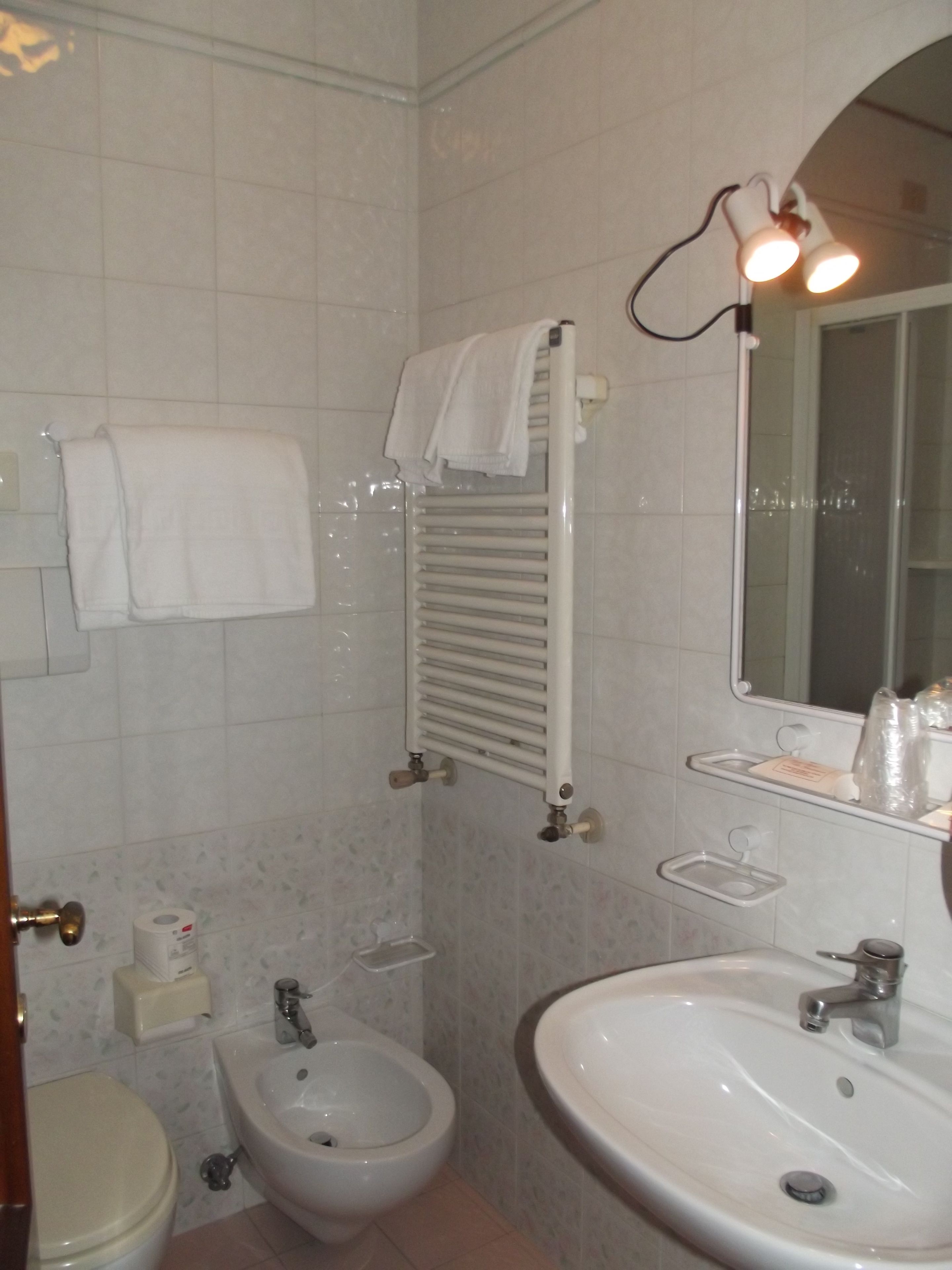 A bathroom with a toilet, bidet, sink, towel rack, and a mirror.