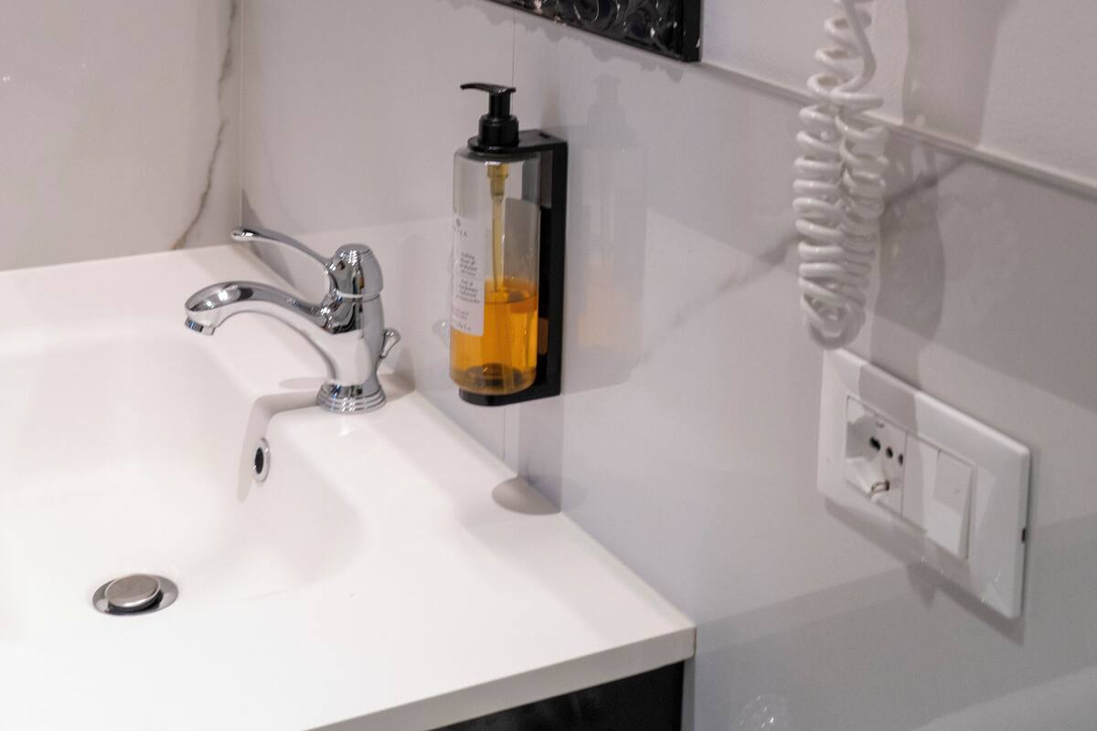 A bathroom with a white sink, a black ornate mirror, and a white hairdryer mounted on the wall.