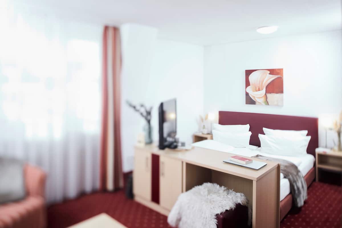 A hotel room with a bed, a desk, a chair, a TV, and a painting on the wall.