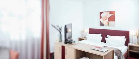 A hotel room with a bed, a desk, a chair, a TV, and a painting on the wall.
