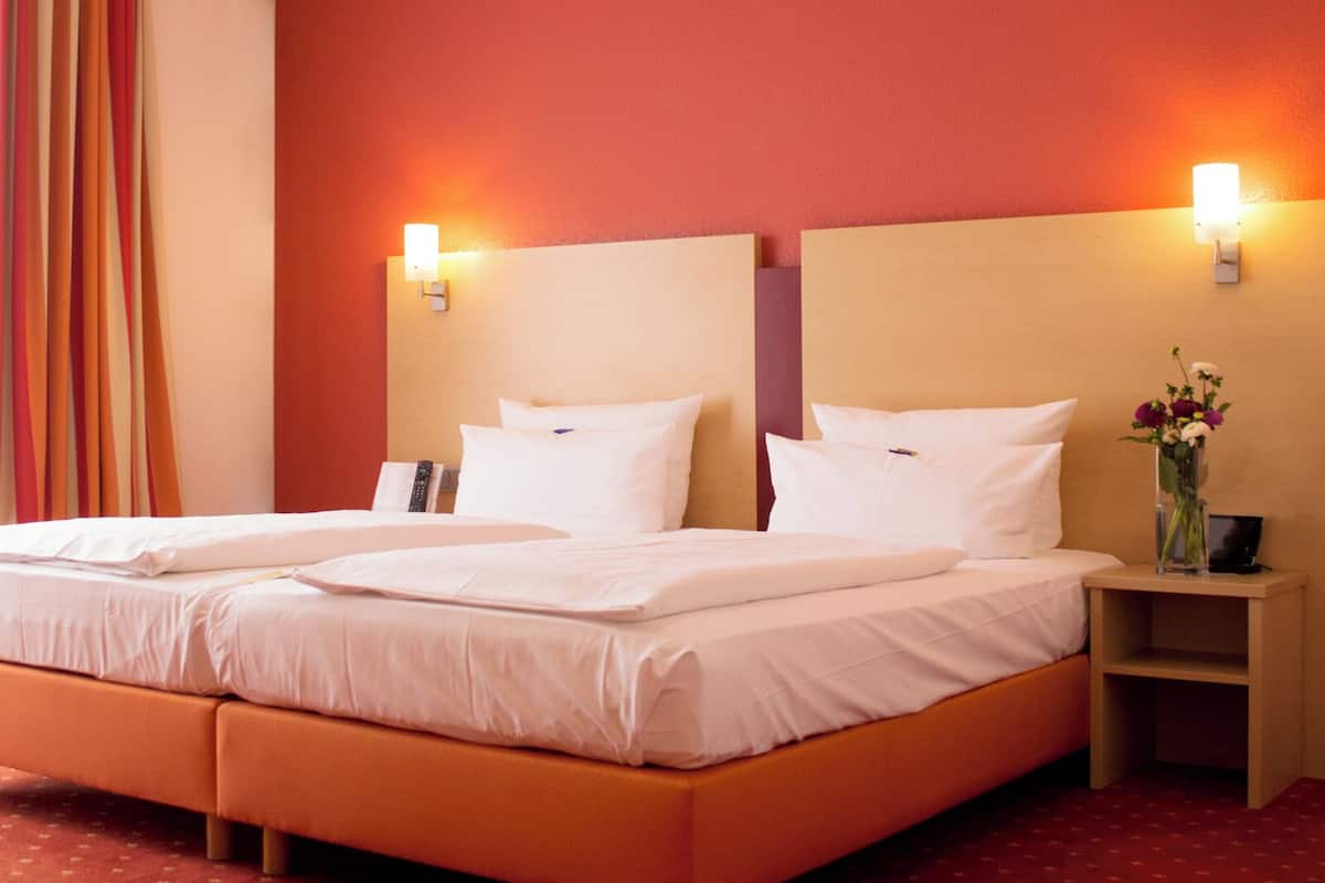 A double bed with white linens, two bedside tables, a vase with flowers, and a wall-mounted phone.