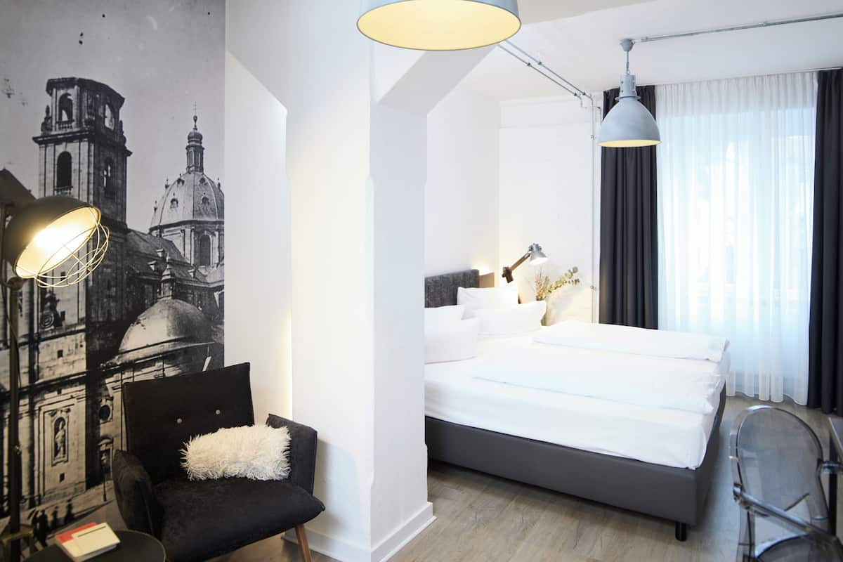 A modern hotel room with a large bed, a desk, a chair, and a wall mural.