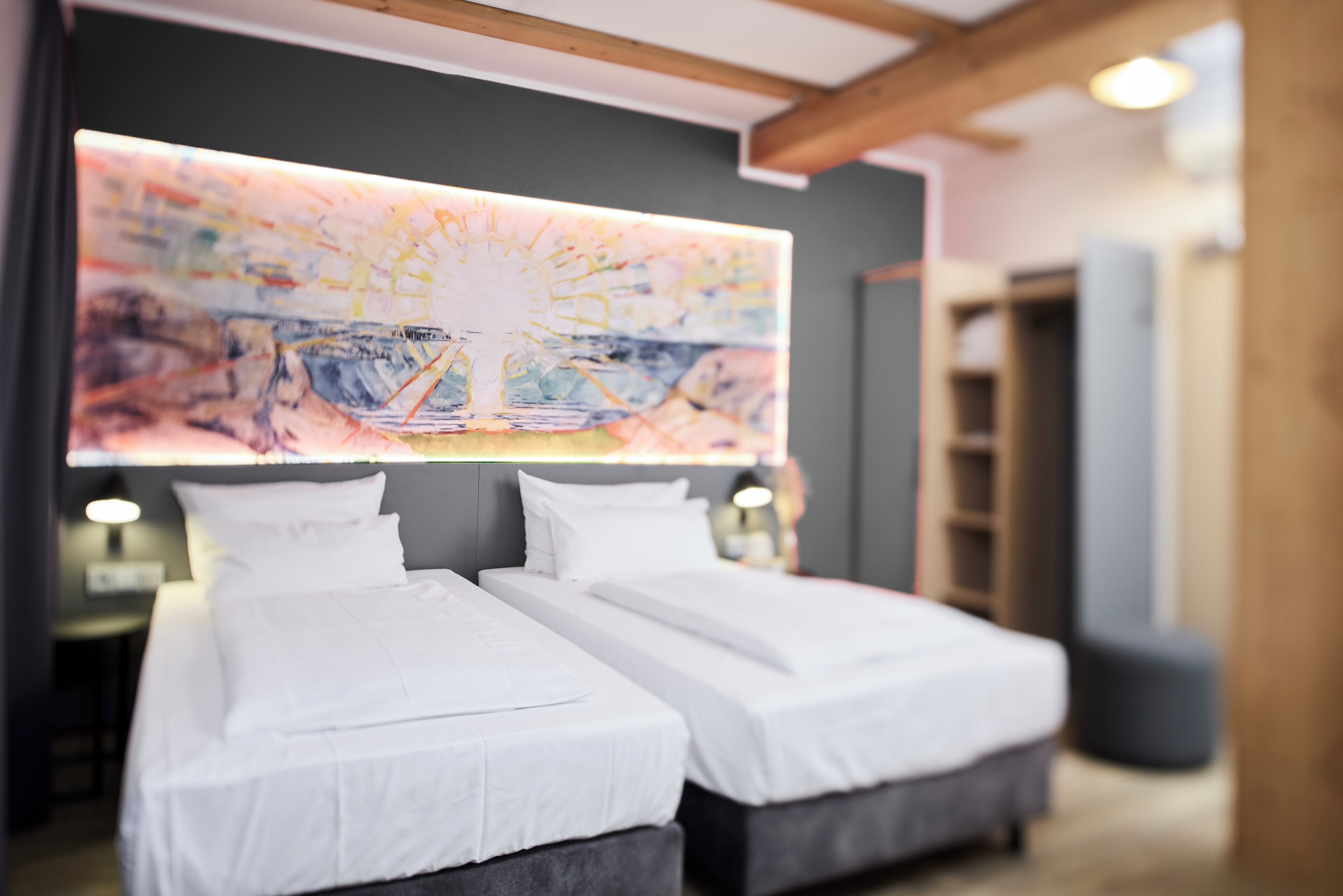 Une chambre d’hôtel avec deux lits, une grande peinture abstraite au mur et un plafond en bois.