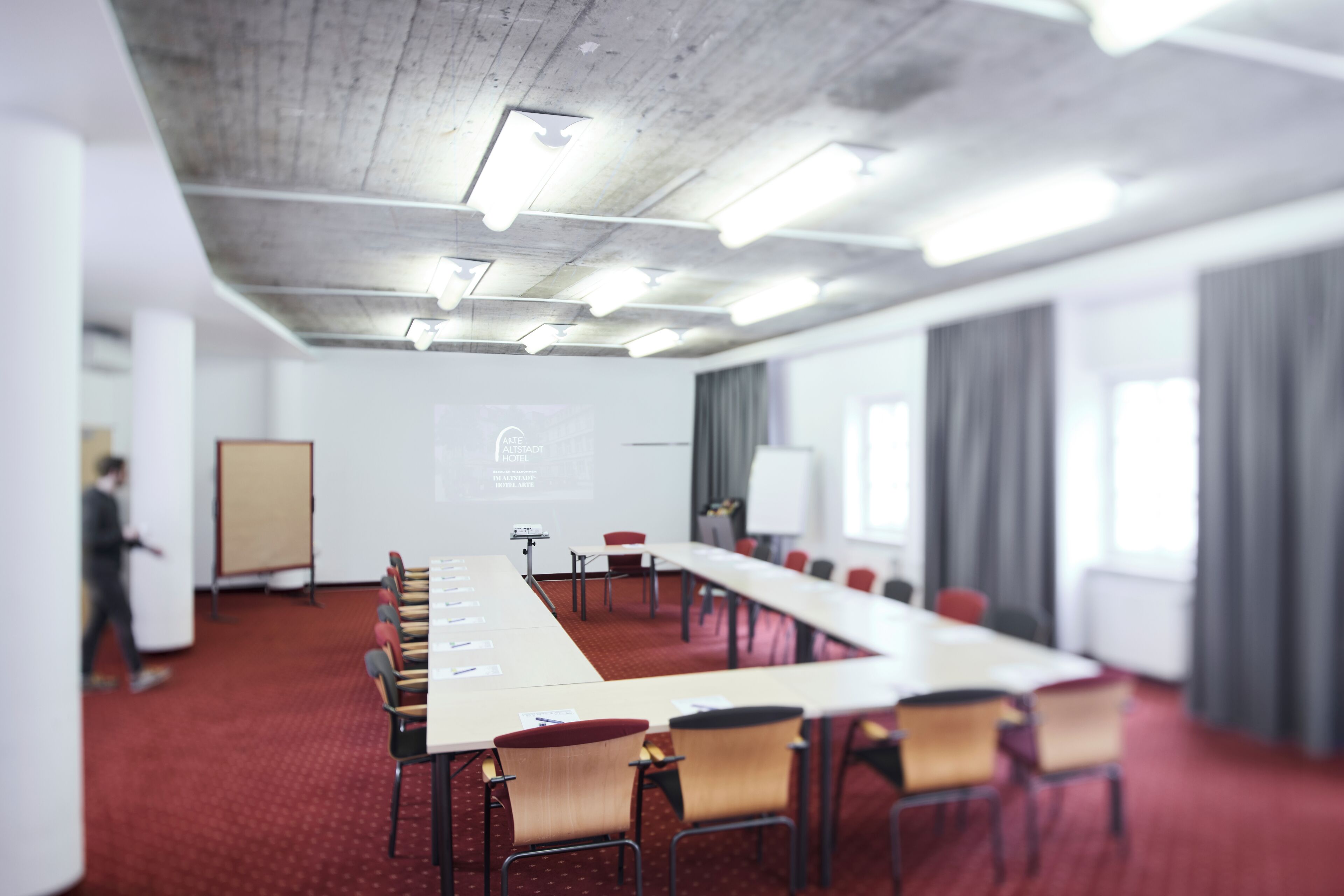 Ein Konferenzraum mit langem Tisch, Stühlen, einer Projektionsleinwand und einer Whiteboard-Tafel.