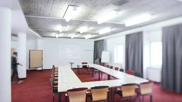 Ein Konferenzraum mit langem Tisch, Stühlen, einer Projektionsleinwand und einer Whiteboard-Tafel.
