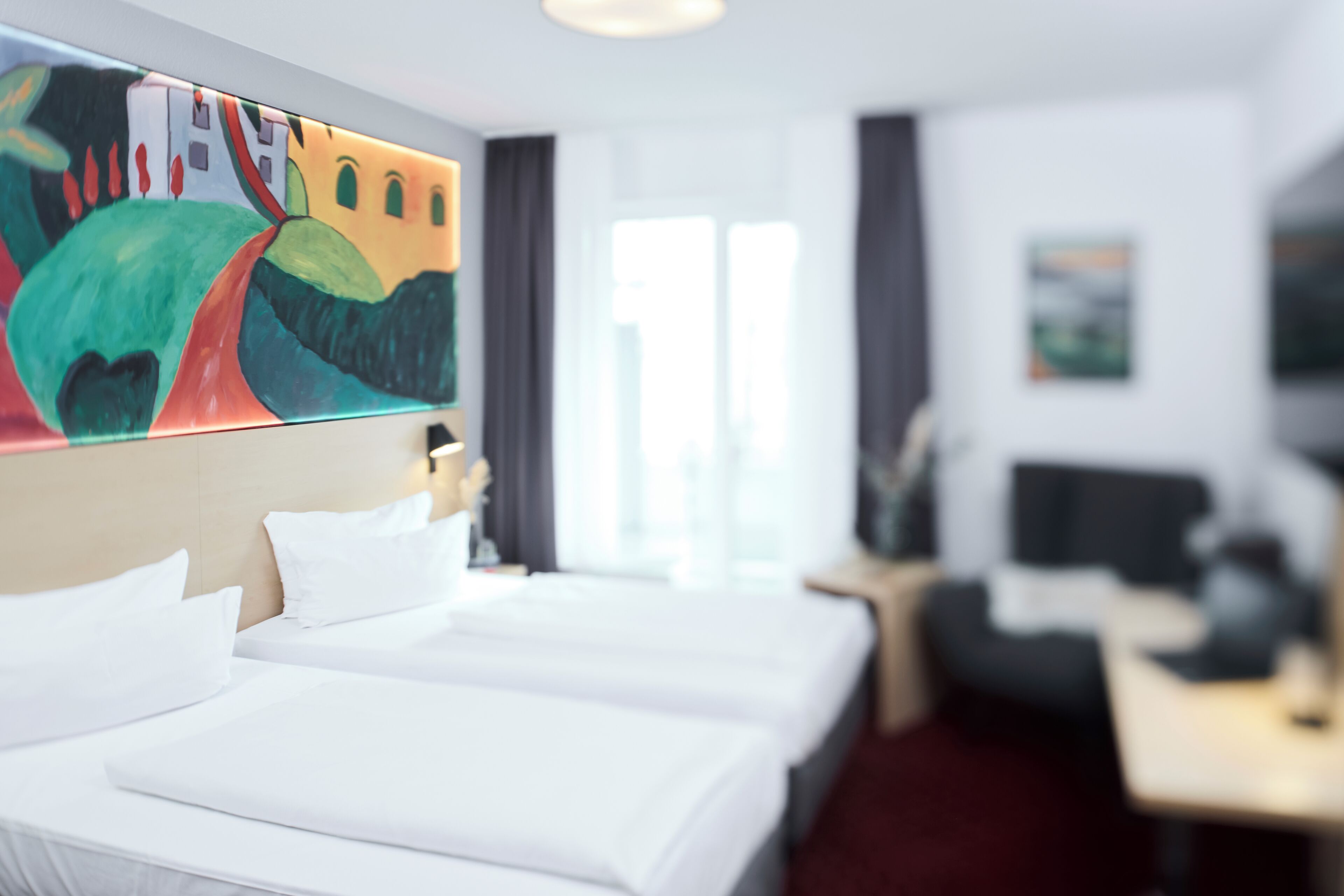 Une chambre d’hôtel avec un grand lit, un bureau, une chaise et un tableau au mur.