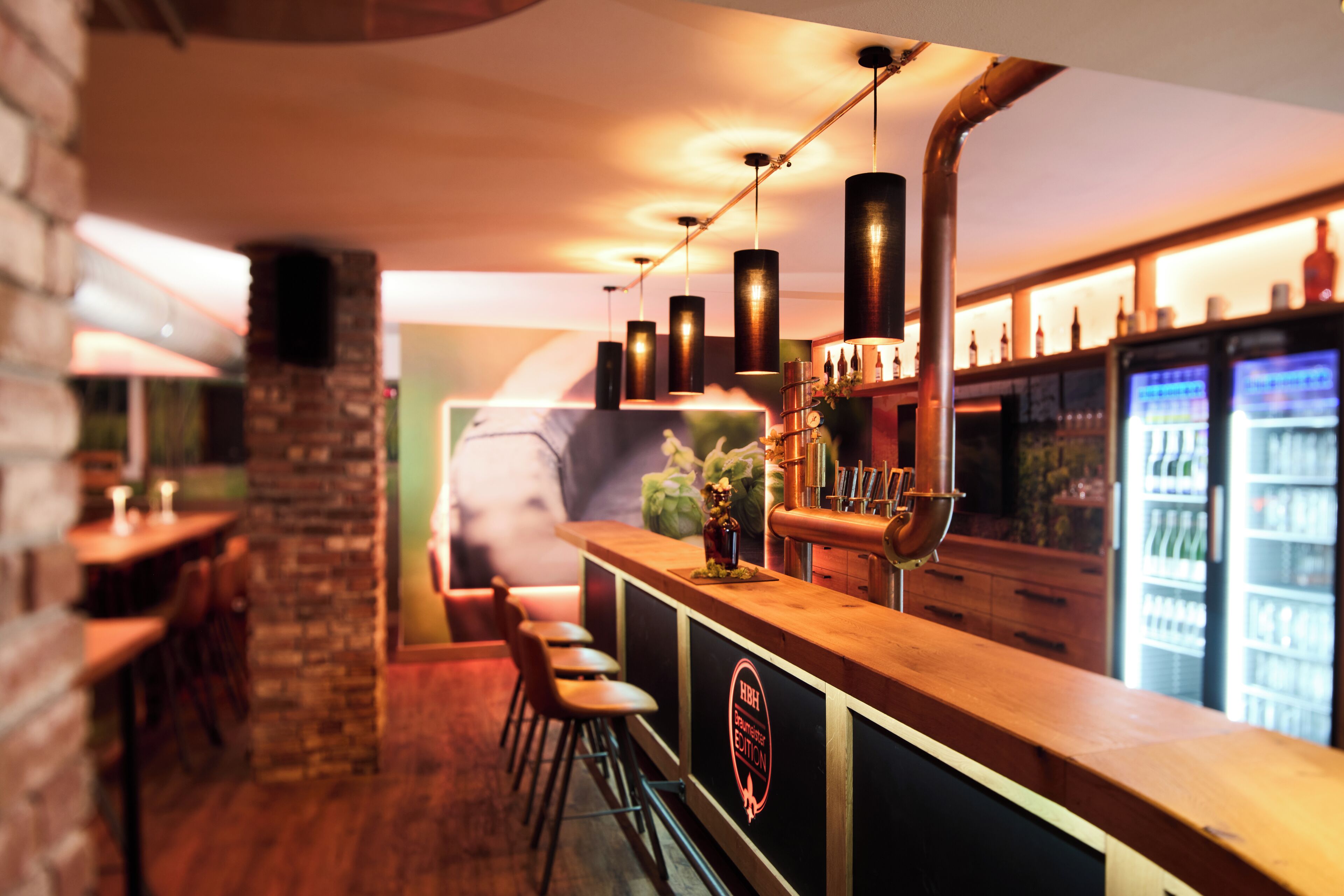 Zona de bar con mostrador de madera, taburetes y grifo de cobre.