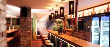 Zona de bar con mostrador de madera, taburetes y grifo de cobre.