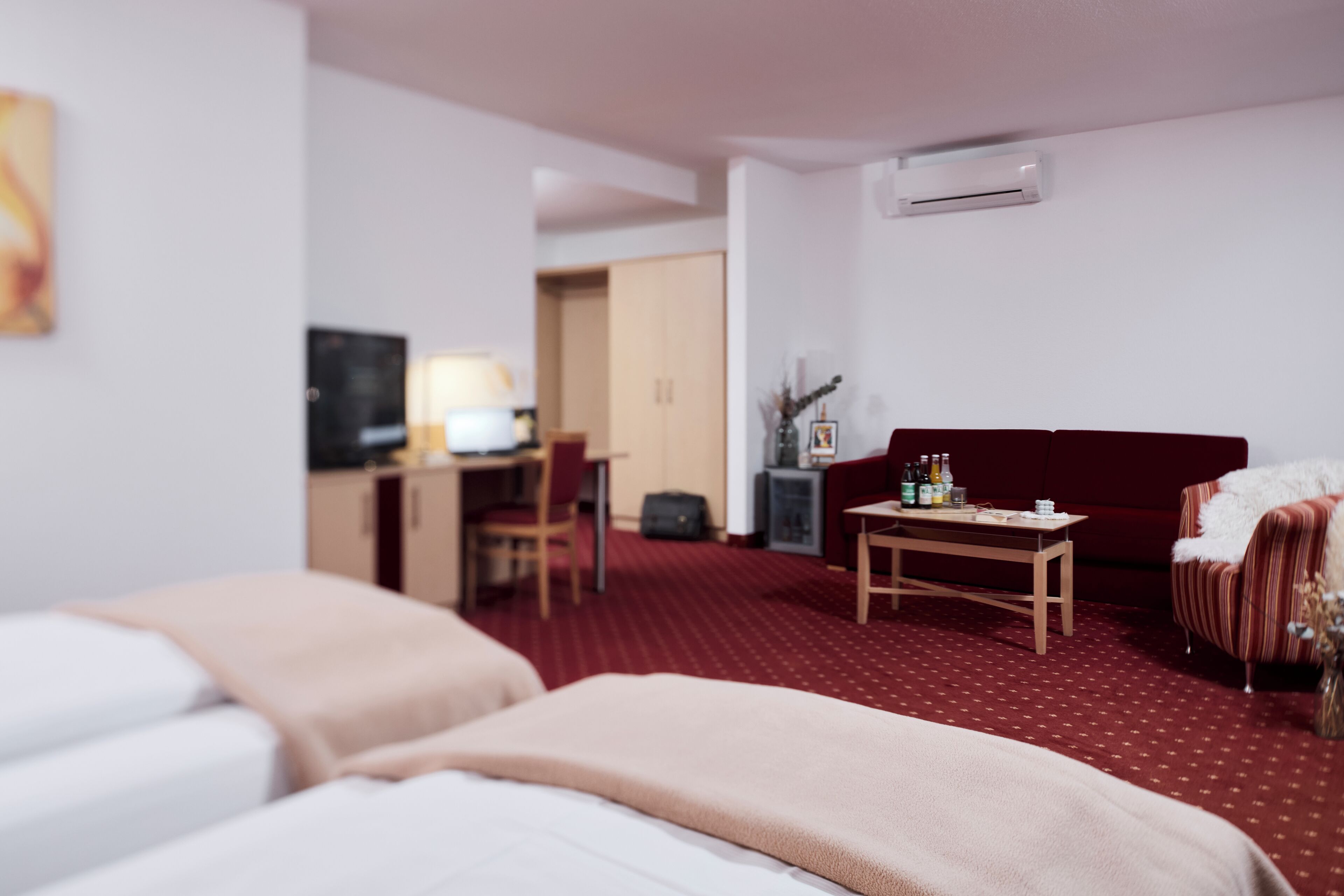 Ett hotellrum med två sängar, ett skrivbord med en dator, en röd soffa och ett litet bord med flaskor.