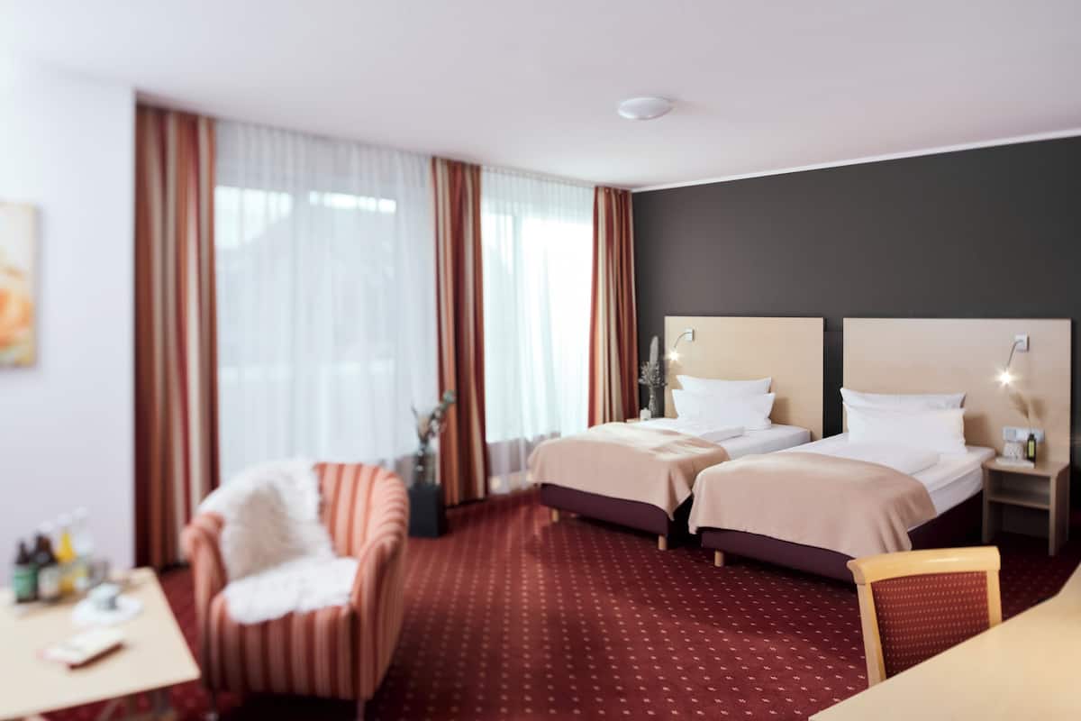 A hotel room with two beds, a desk, a chair, and a large window with curtains.