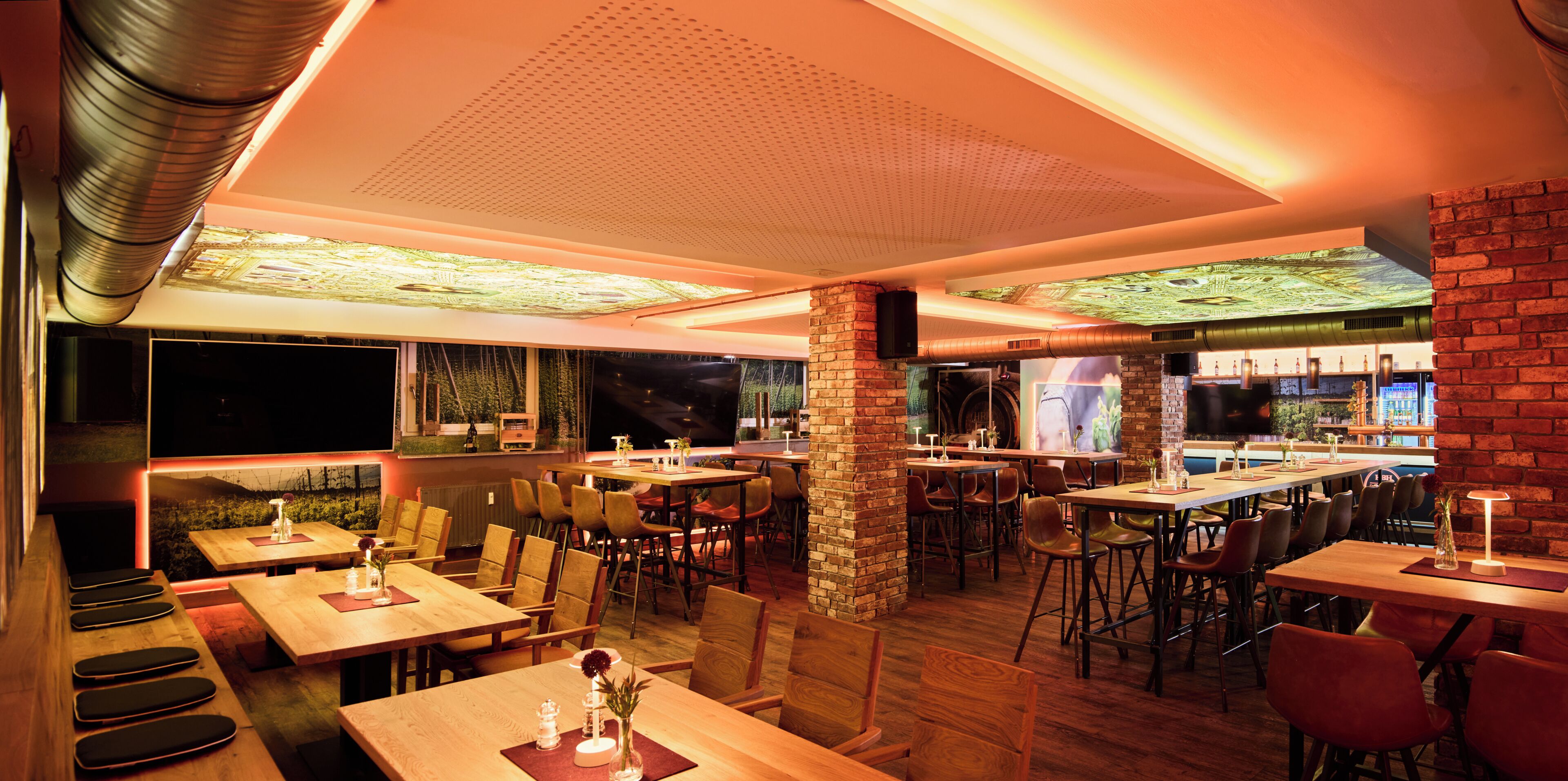 A restaurant interior with multiple tables and chairs, a brick column, and a bar area.