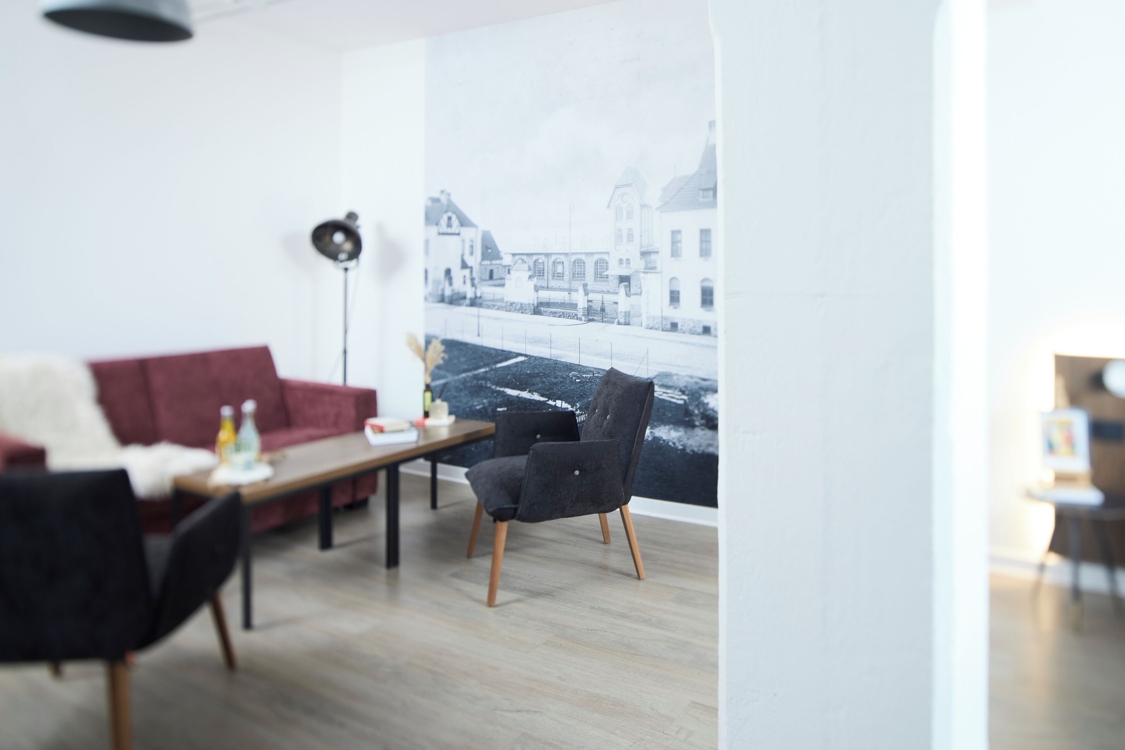 Ein modernes Wohnzimmer mit einem roten Sofa, einem schwarzen Sessel, einem Holztisch und einer Stehlampe.