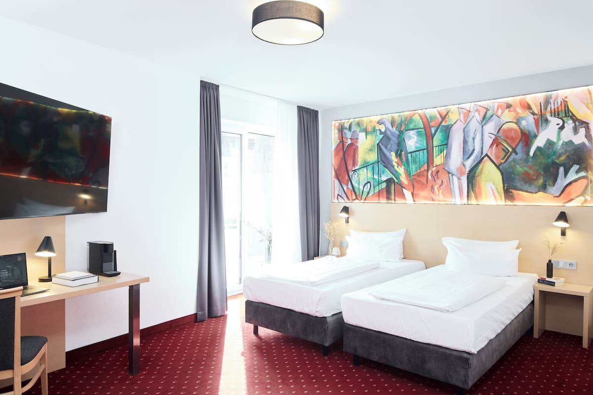 A hotel room with two beds, a desk with a computer, a TV, and a large abstract painting.