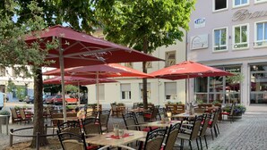 Café al aire libre con sombrillas rojas, sillas de mimbre y mesas.