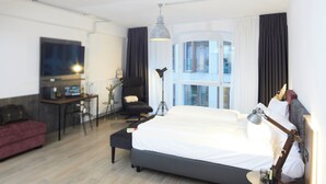Una habitación de hotel moderna con una cama grande, un escritorio con silla, un sofá y un ventanal con cortinas.
