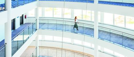 A multi-level atrium with glass railings, a central walkway, and a person walking.