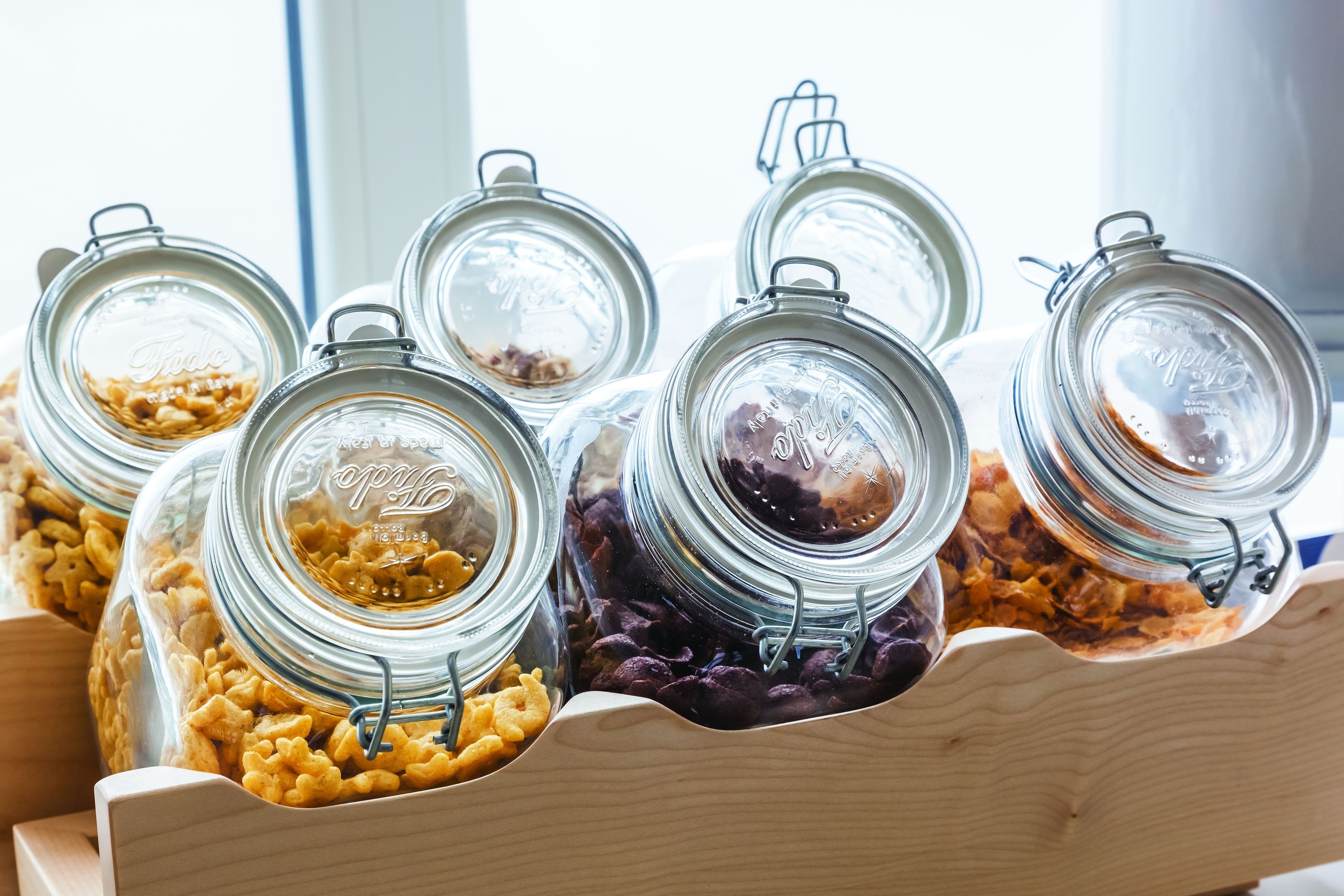 Una bandeja de madera con varios frascos de vidrio y tapas metálicas, que contienen diferentes tipos de alimentos.