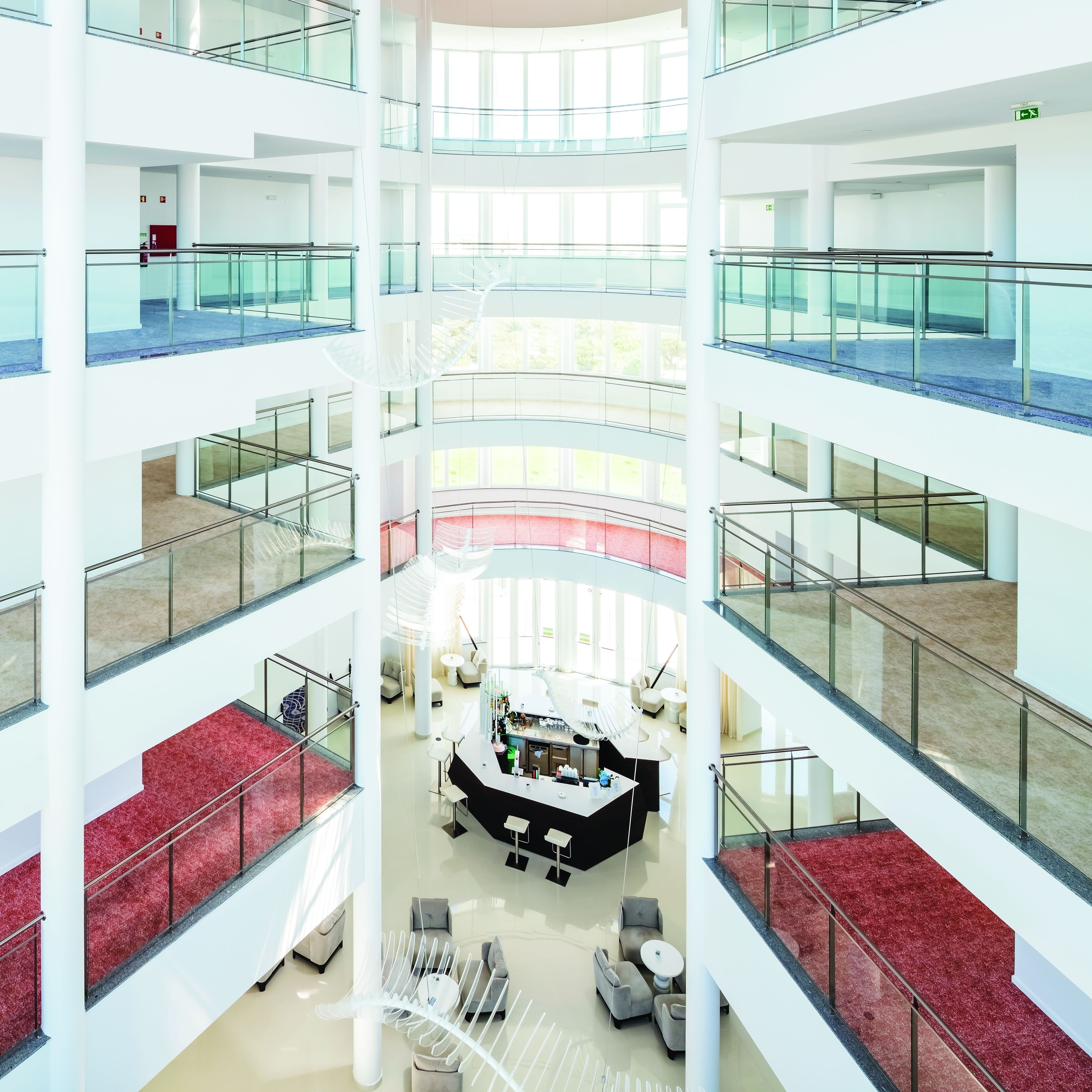 A multi-level atrium with glass railings, a central seating area, and a red carpeted staircase.